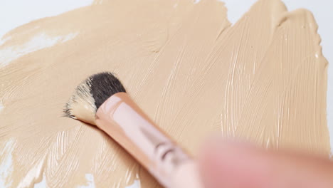 brushing a nude colored concealer on a clean, white board using a small wand applicator