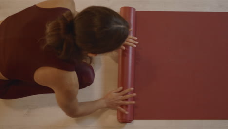 mujer enrollando colchón de fitness después de hacer ejercicio. niña doblando colchón de yoga en el estudio