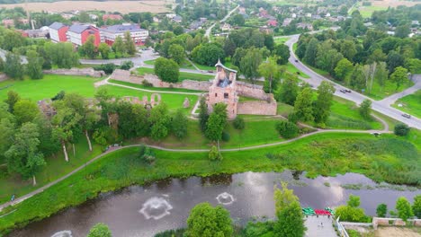 aerial view of dobele castle ruins, flowing berze river and illuminated fountains at sunset serene latvian summer evening from above, scenic aerial of latvian historical landscape in golden hour