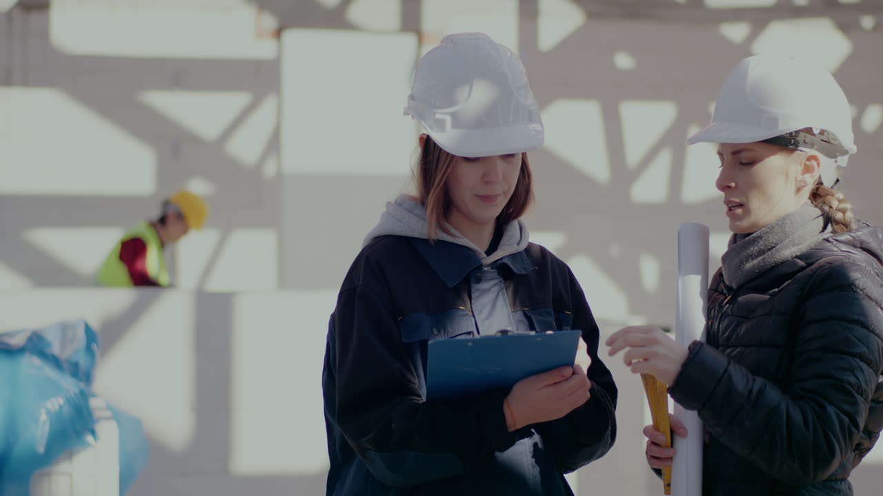 Young female architect gesturing while explaining to engineer standing with clipboard at construction site