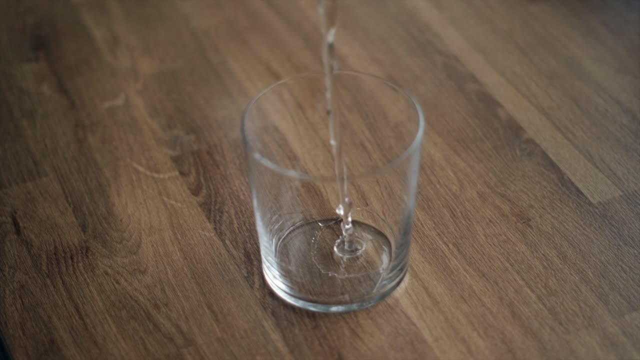 Super Slow Motion of Water Being Poured Into a Glass on a Wooden Table