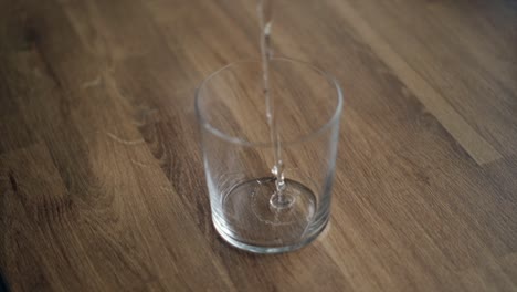 super slow motion of water being poured into a glass on a wooden table