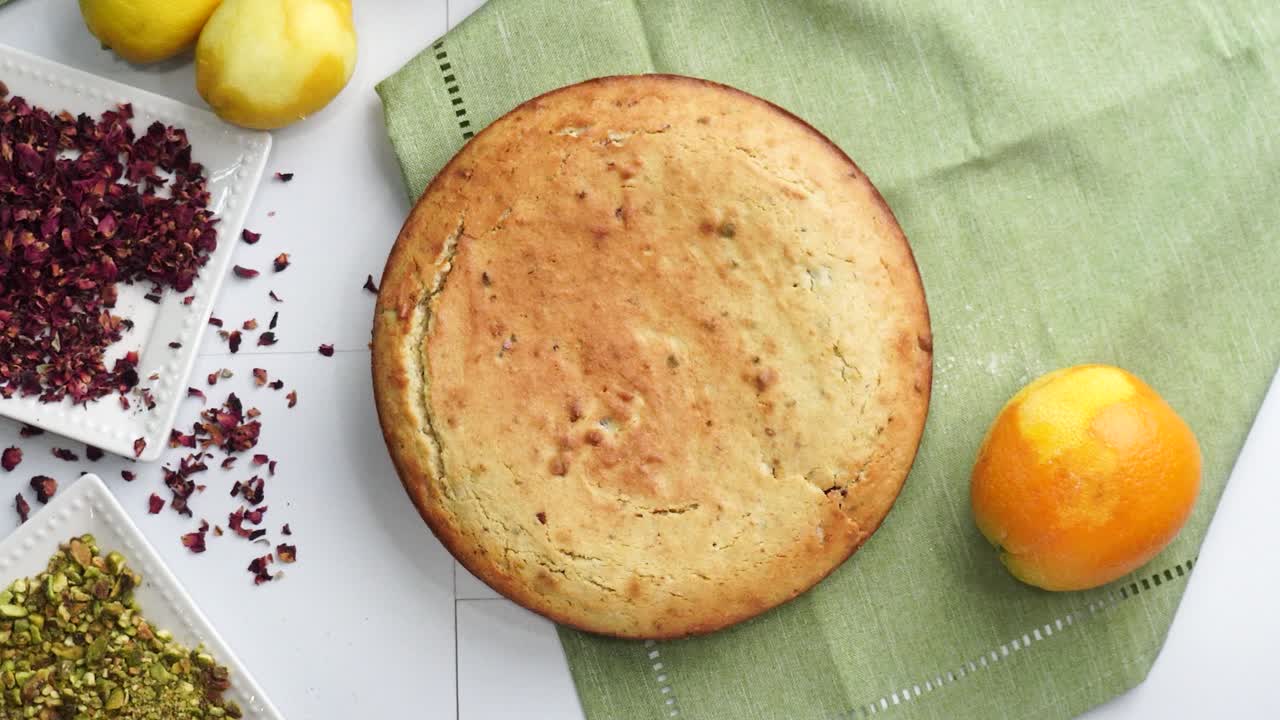 Baking a dessert called Persian Love Cake made with rose petals and pistachios. Cake with white glaze frosting. Moving the Persian Love cake off the table. Beautiful cake for tea time or celebration