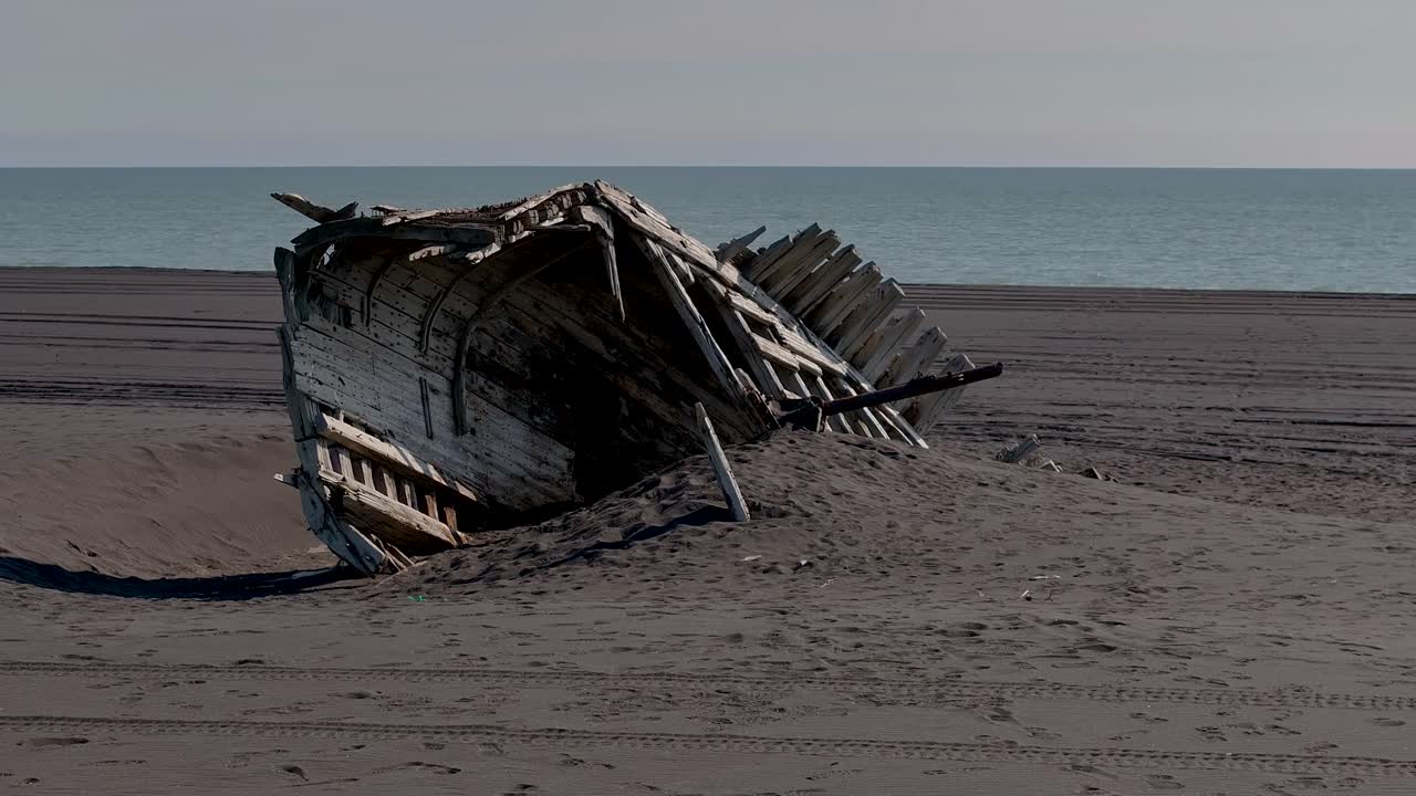 Wooden Shipwreck Isolated In The Black Sand Beach In Vestmannaeyjar, Iceland. Aerial Orbiting Shot