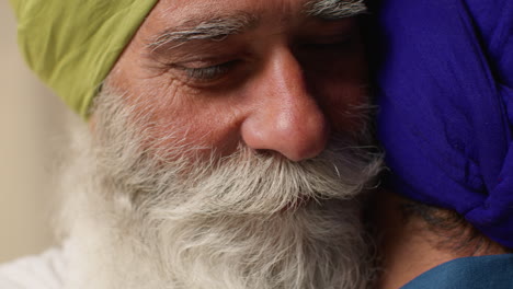 close up studio shot of senior sikh father embracing adult son both wearing turbans against plain background 1