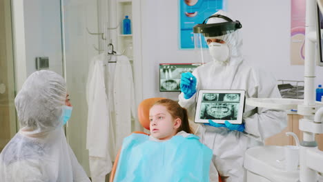 dentist with face shield explaining panoramic mouth x-ray image to mother of kid