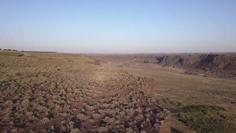 Aerial-rises-to-sagebrush-plateau-above-wide-coulee-canyon-walls