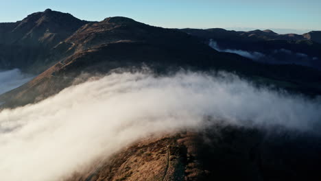 Nebelige-Berge-Mit-Sonnenbeschienenen-Gipfeln-Und-Tälern,-Wolken-Ziehen-In-Einer-Luftaufnahme-über-Die-Landschaft