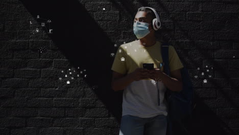 animation of icons over biracial man using smartphone with face mask