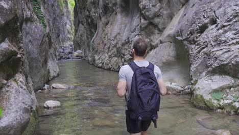 Curious-young-man-walking-along-stream-in-canyon.