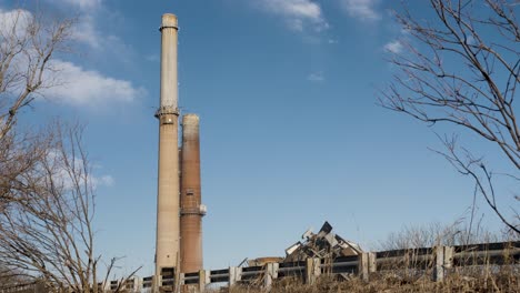 old coal-fired power plant smoke stacks against a blue sky with trees and road in foreground, demolished building