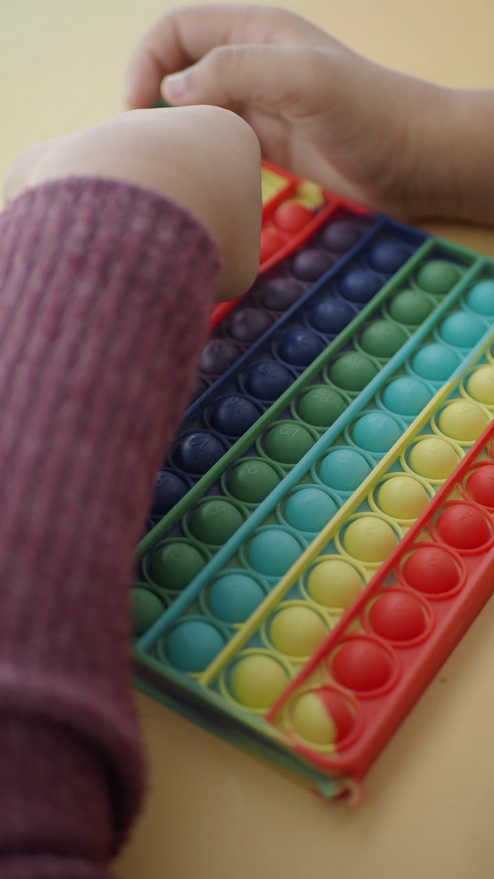 Child's Hands Playing with Rainbow Pop It Fidget Toy