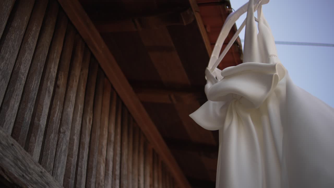 Wedding dress gently swaying on a wooden structure against a clear sky