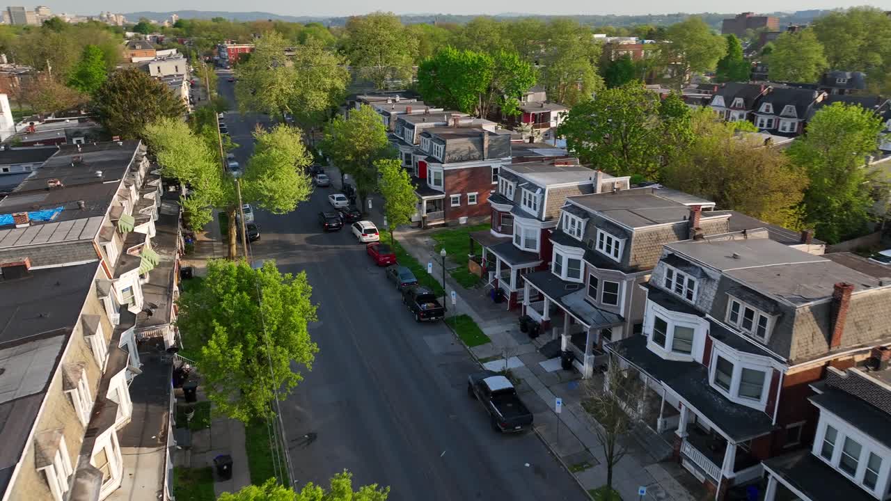 Aerial footage of a quiet residential neighborhood with tree-lined streets, charming row houses, and parked cars