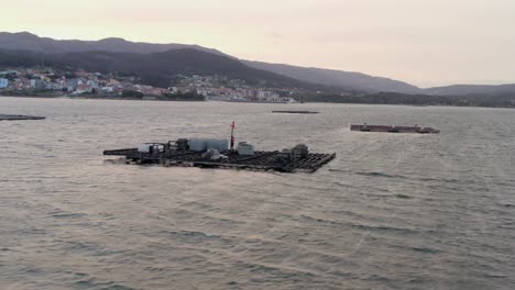 Toma-Cinematográfica-De-Batea-De-Cultivo-De-Mejillones,-Fondo-De-Silueta-De-Montaña