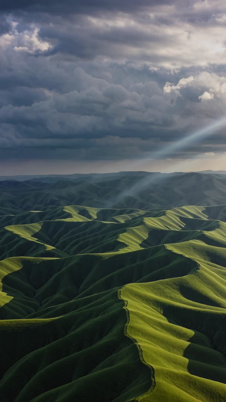 Aerial view of lush green hills under dramatic clouds, with sun rays piercing through