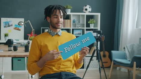 man holding "follow me" sign in home studio