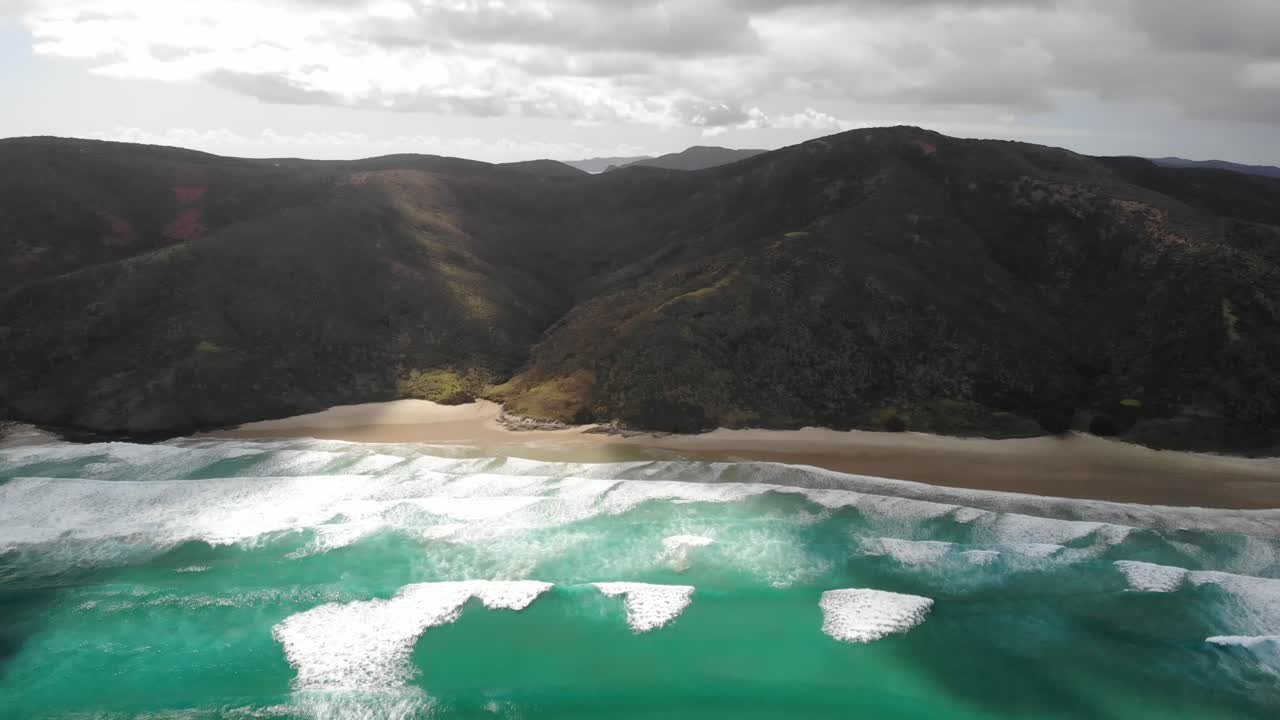 Dron letící směrem k hoře a pobřeží u pláže Te Werahi, Cape Reinga