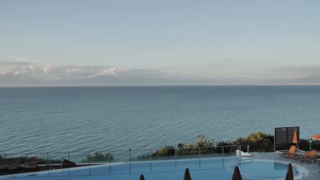 wide tilting shot of a coast view from the beautiful swimming pool to deep-sea with some mountains in the background