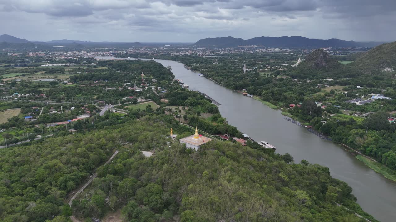 Stunning wide-angle aerial drone shot of a golden pagoda perched atop a lush hilltop in Saraburi Province, central Thailand