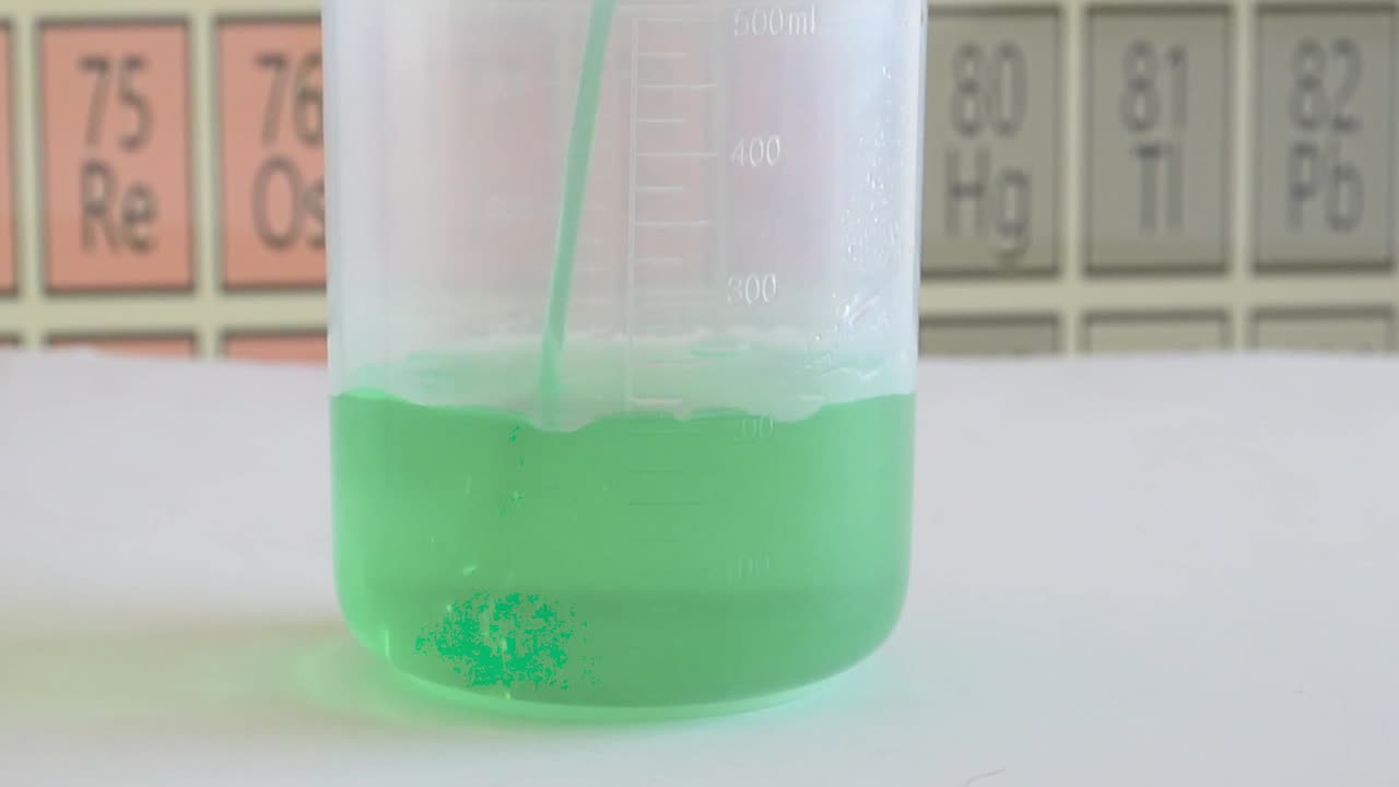 Chemical solution is being poured into a beaker with the periodic table in background.