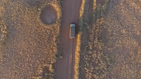 4k straight down high aerial view of a 4x4 safari vehicle driving on a sand track through the african savannah grasslands with the famous fairy circles, namibia