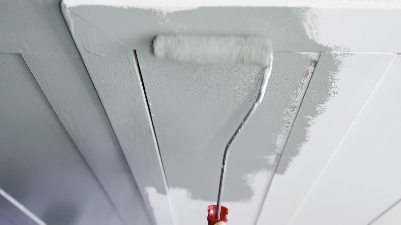 Een close-up van een verfroller die een laag grijze verf aanbrengt op een gladde witte muur, met vers geschilderde streken.