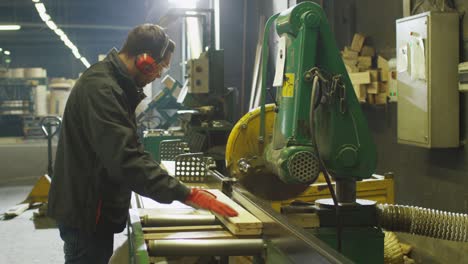 lumber mill worker is cutting wood with circular saw.