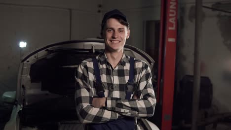 Portrait-of-young-handsome-car-mechanic-in-workshop,-in-the-background-of-service.-Car-repair,-fault-diagnosis,-technical-maintenance-concept.