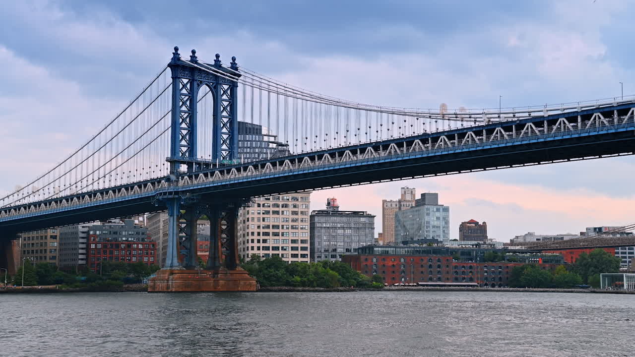 Train moves by the Manhattan Bridge. Low angle view at the structure from the East River waterscape