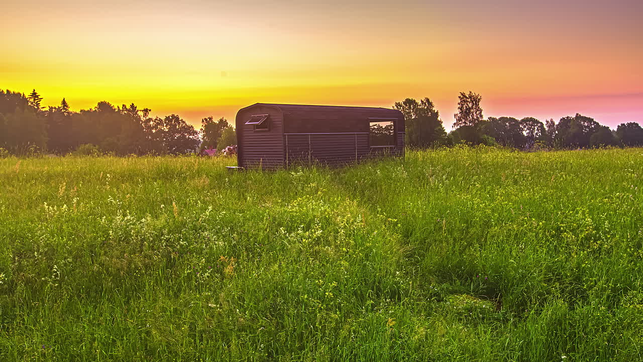 lapso de tiempo de la hoguera al lado de la cabaña de madera durante la noche y el sol se eleva en el cielo al amanecer sobre el campo rural
