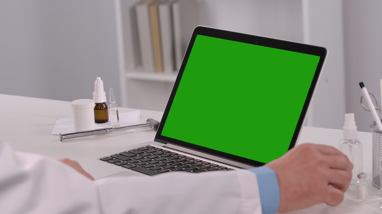 el médico masculino consulta al paciente usando una computadora portátil con pantalla verde y demuestra el vial con la vacuna. consulta remota en línea sobre la necesidad de vacunación. telemedicina. de cerca. cámara lenta