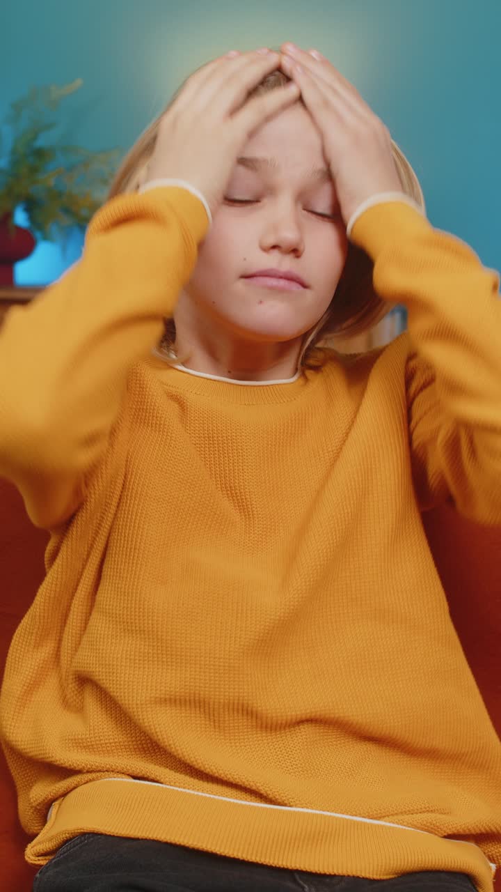 Ragazzo adolescente che tiene la testa con un'espressione stressata che pensa profondamente dopo una brutta giornata seduto sul divano a casa