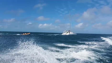 velero navegando en el mar caribe con bote atado detrás, olas y agua salpicada