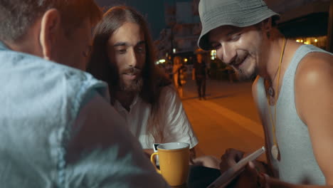 man is showing his friends something in white tablet computer in summer cafe at night thessaloniki greece