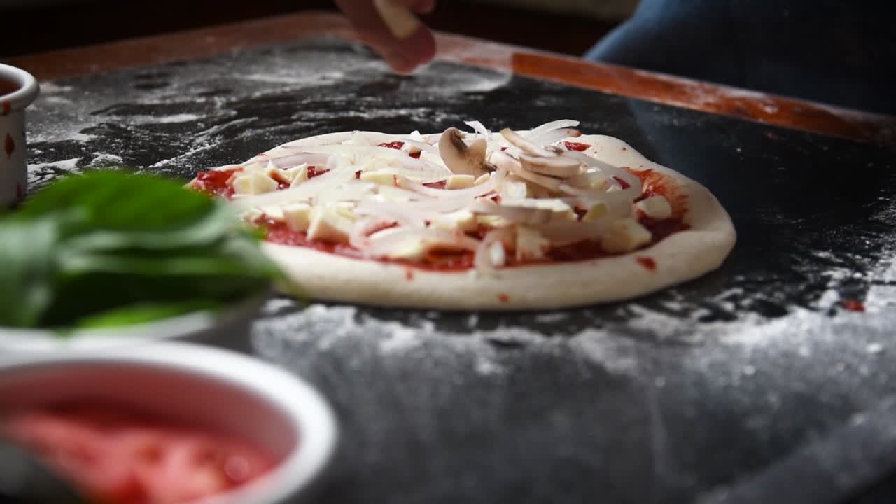 요리사가 살사 양파와 모짜렐라 치즈를 곁들인 집에서 만든 사워도우 피자에 버섯을 얹고 있습니다.