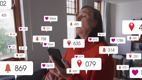 Animation-of-social-media-icons-over-caucasian-senior-woman-sneezing-while-using-smartphone-at-home