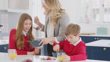 mother wearing business suit having breakfast with children in school uniform before work