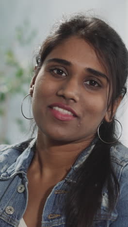 happy indian woman takes off glasses looking in camera with smile on face. portrait of brunette lady with ponytail on blurred background closeup