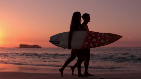 una pareja linda caminando por la playa con una tabla de surf.