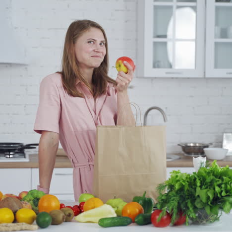 lovely woman with fresh apple at home. organic fruit and vegetables on the kitchen table and young female holding an apple. healthy food.
