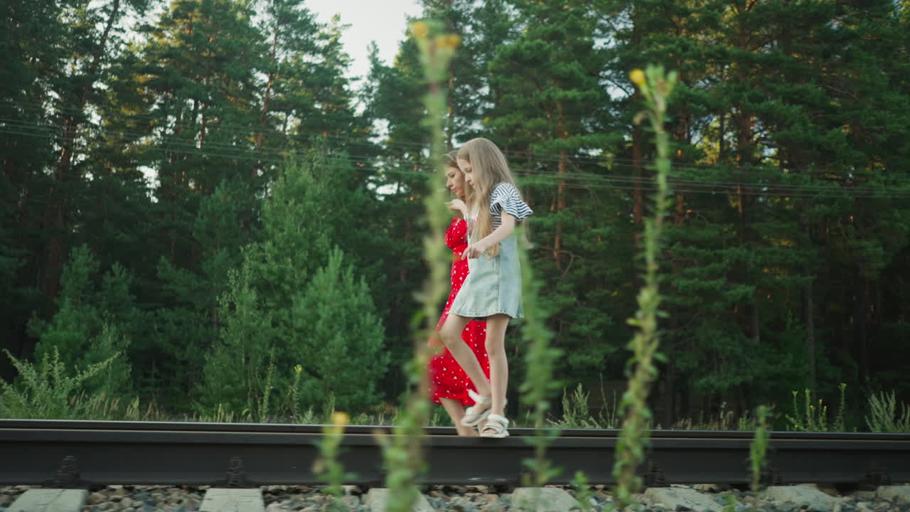 side view of young woman holding little girl hand as she walks on rail beam with careful balance, forest trees in background, moment filled with care, nature, and connection between generations
