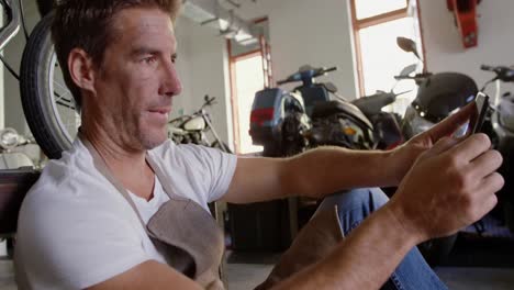 mecánico masculino usando teléfono móvil en el garaje de reparación de motocicletas 4k