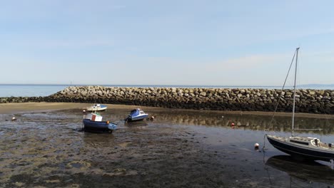 aerial low angle view boats in shimmering low tide sunny warm rhos on sea seaside sand beach marina pill back reverse right