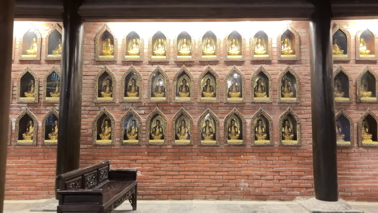Sala interna del tempio presso la Pagoda di Bai Dinh a Ninh Binh, Vietnam, caratterizzata da grandi pilastri di legno e pareti rivestite con piccole nicchie dorate di Buddha.