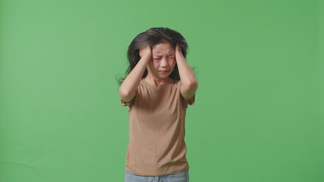 young asian woman victim of violence with bruise on face having nervous breakdown and screaming on green screen background in the studio