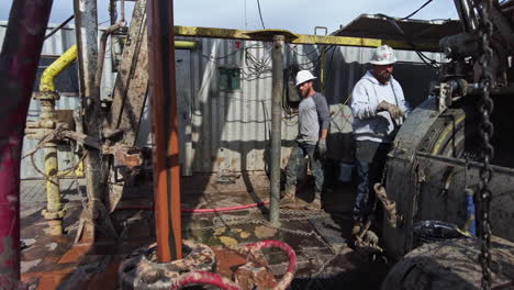 long metal pole is rising at the drilling site. men in protective helmets work at the derrick for producing oil.