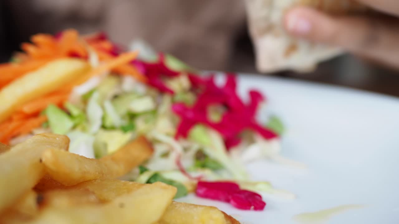 primer plano de una persona comiendo un envoltorio de pollo con papas fritas y una ensalada