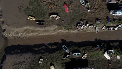 Various-stranded-abandoned-fishing-boat-wreck-shipyard-in-marsh-mud-low-tide-coastline-aerial-pull-back-birdseye-view