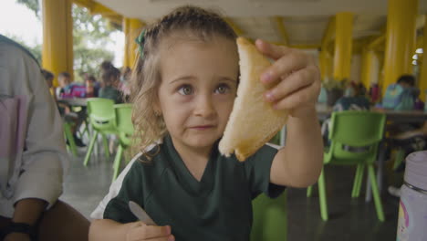 ein blondes mädchen genießt spielerisch ein stück brot in einer cafeteria, ihre lustigen ausdrücke und freudige energie erfassen einen lustigen und sorglosen frühstücksmoment